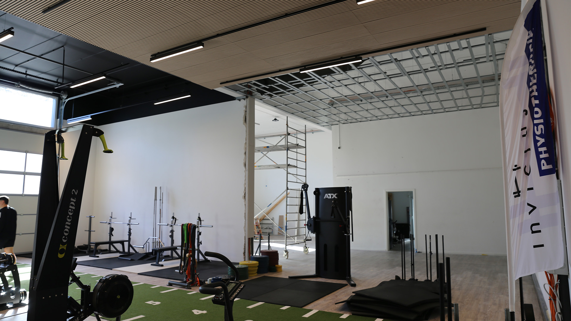 Blick aus Trainingshalle 1 durch den Wanddurchbruch in die neue Halle 2, dort noch Gerüst und offene Deckenunterkonstruktion.